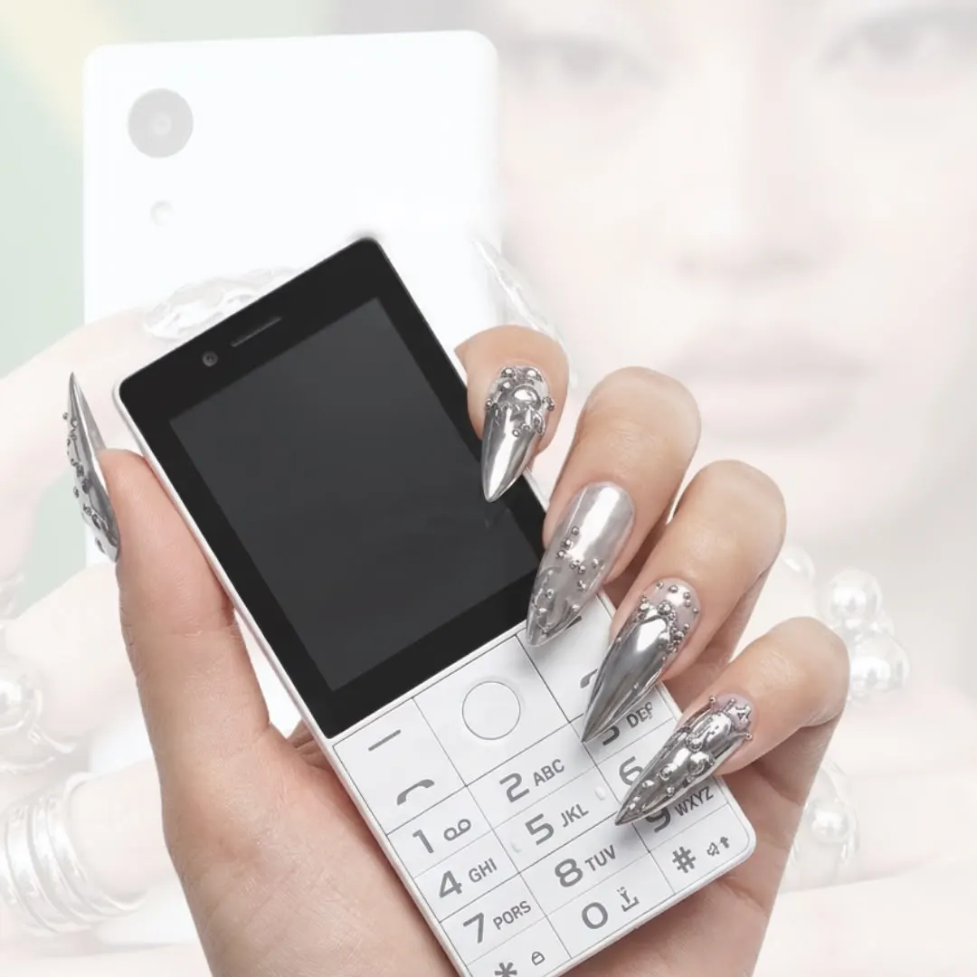 Hand with chrome nails holding the white Caytonia Phone with its classic keypad